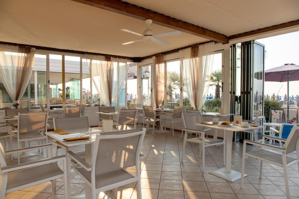 un restaurant avec des tables et des chaises blanches et des fenêtres dans l'établissement Hotel Telenia, à Lido di Jesolo