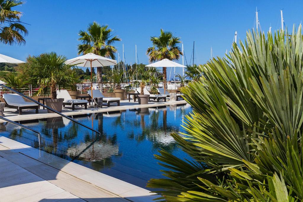 une piscine avec chaises longues, parasols et palmiers dans l'établissement Marina di Scarlino Resort, à Puntone di Scarlino