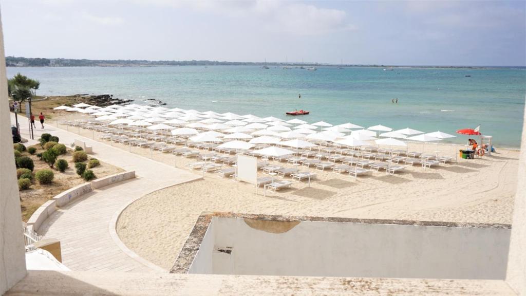 - une plage avec un bouquet de parasols blancs et l'océan dans l'établissement Hotel Riva Del Sole, à Porto Cesareo