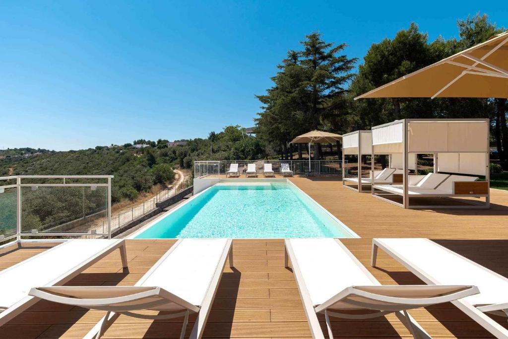 - une piscine avec des chaises blanches et un parasol dans l'établissement Trullo Ad Caelum, à Fasano