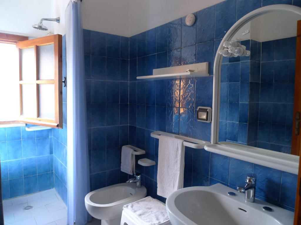 La salle de bains est pourvue de carrelage bleu, de toilettes et d'un lavabo. dans l'établissement Hotel Alexander, à Tropea