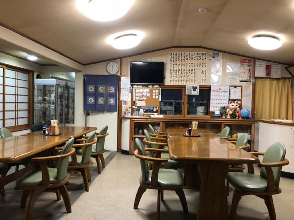un restaurant avec des tables et des chaises en bois et une télévision dans l'établissement Minshuku Kawarabi-so, à Nosegawa