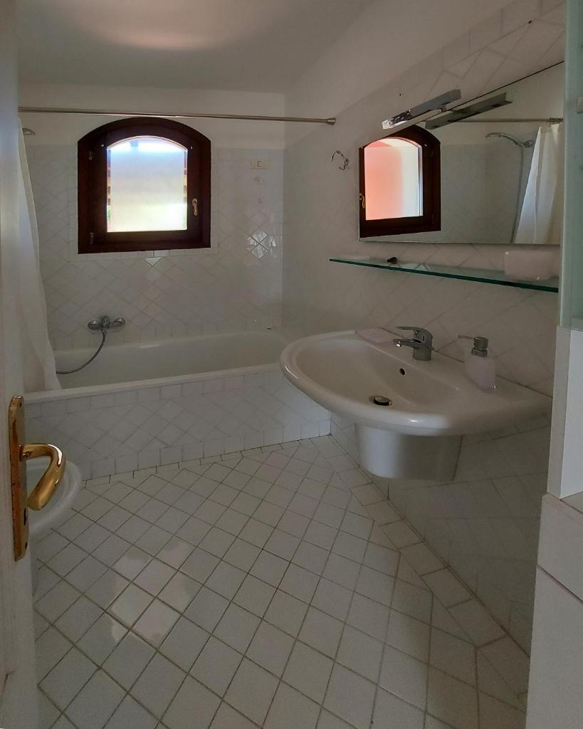 La salle de bains blanche est pourvue d'un lavabo et d'une baignoire. dans l'établissement Villa Venere, à Stintino