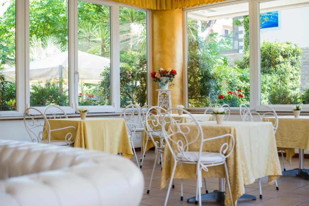 un ensemble de tables et de chaises dans une pièce avec fenêtres dans l'établissement Hotel Sylvia, à Lido di Camaiore