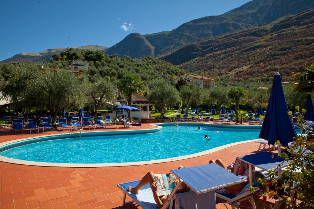 une piscine avec des chaises et des montagnes en arrière-plan dans l'établissement Club Hotel Olivi - Tennis Center, à Malcesine