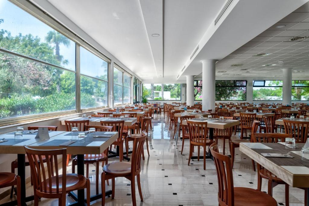 une salle à manger avec tables, chaises et fenêtres dans l'établissement Nicolaus Club La Giurlita, à Ugento