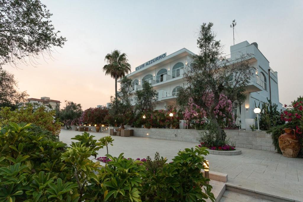 un bâtiment avec des arbres et des fleurs devant lui dans l'établissement Club Azzurro Hotel & Resort, à Porto Cesareo