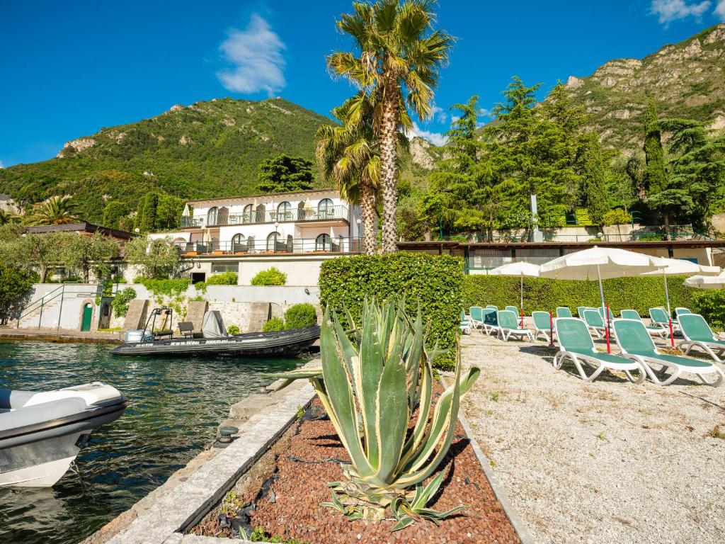 un groupe de chaises et de palmiers à côté d'une masse d'eau dans l'établissement Hotel Leonardo Da Vinci, à Limone sul Garda