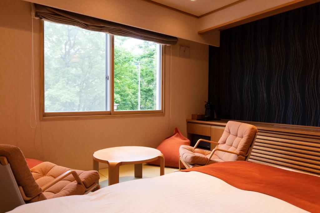- une chambre avec deux chaises, un lit et une fenêtre dans l'établissement Kyukamura Shikotsuko, à Chitose
