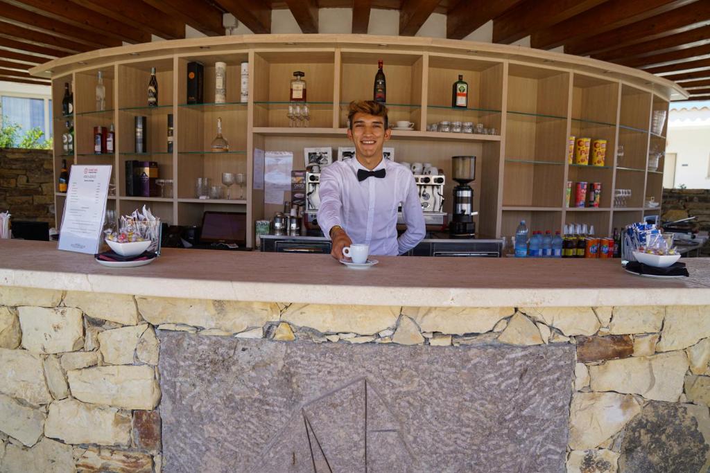 un homme debout derrière un comptoir dans un bar dans l'établissement GH Santina Resort & SPA, à Valledoria 51 autres photos