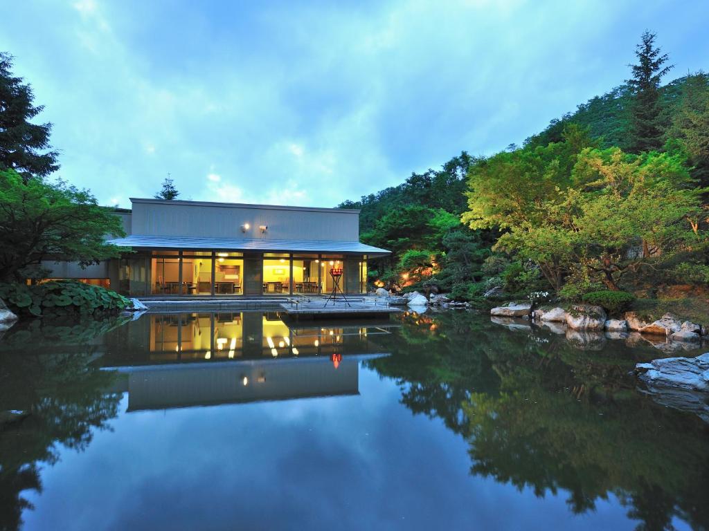 une maison au bord d'une rivière avec ses lumières allumées dans l'établissement Hotel Kazuno, à Kazuno