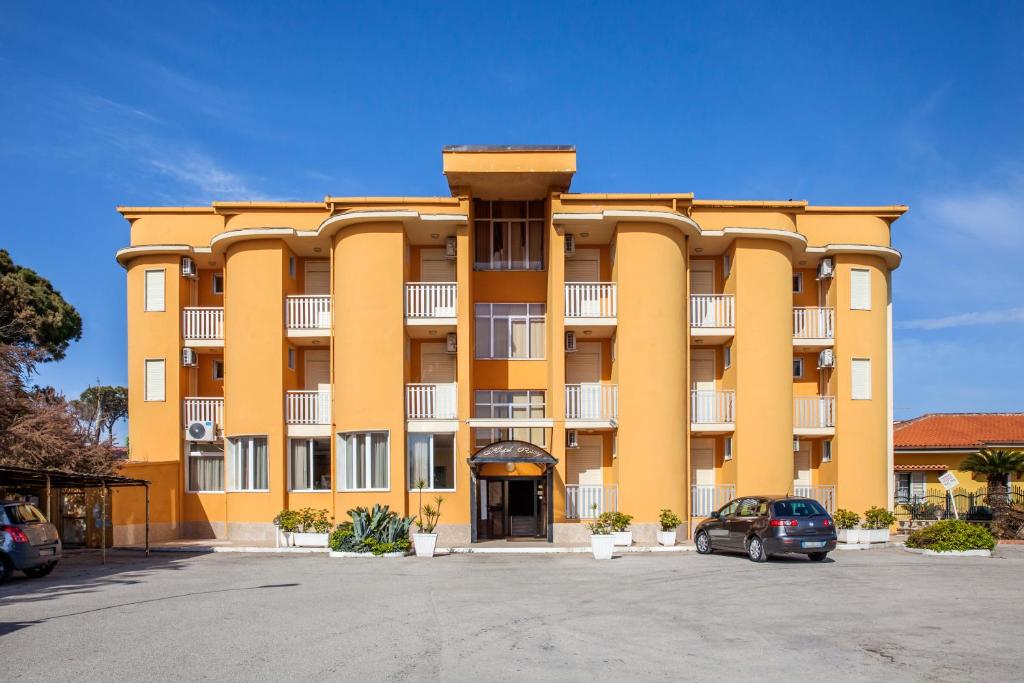 un grand bâtiment jaune avec une voiture garée dans un parking dans l'établissement Hotel Rosy, à Battipaglia