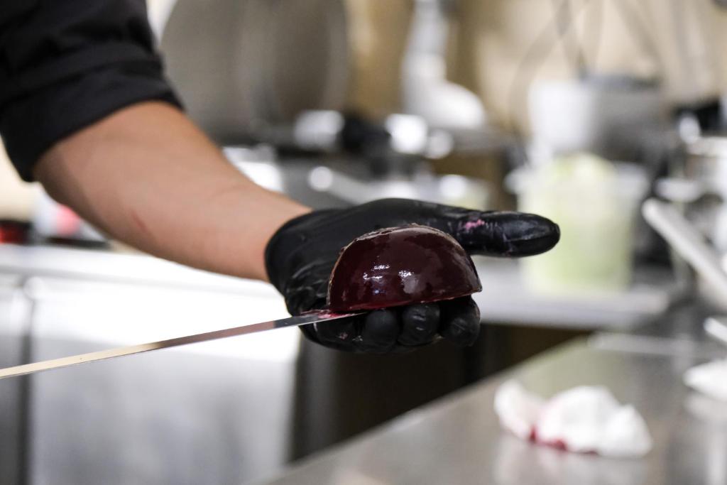 une personne portant des gants noirs tenant un dessert au chocolat sur un bâton dans l'établissement Hotel Delle Mimose, à Lido di Jesolo
