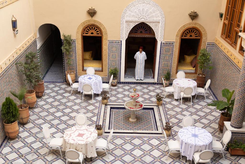 un homme debout dans une cour avec des tables et des chaises dans l'établissement Riad Sayeda Al Hora, à Fès