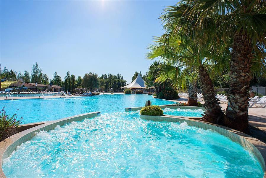 une grande piscine avec de l'eau bleue et des palmiers dans l'établissement Mobil-Home - Les Terrasses Vias Plage, à Vias
