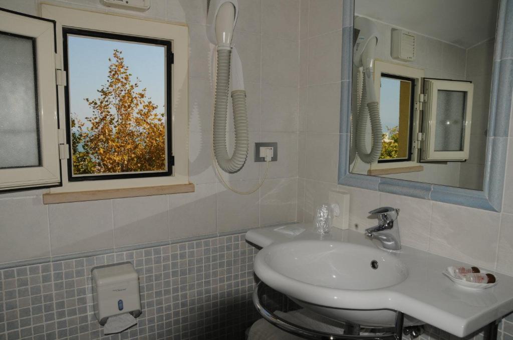 La salle de bains est pourvue d'un lavabo et d'un arbre dans la fenêtre. dans l'établissement Hotel Corallo, à Francavilla al Mare