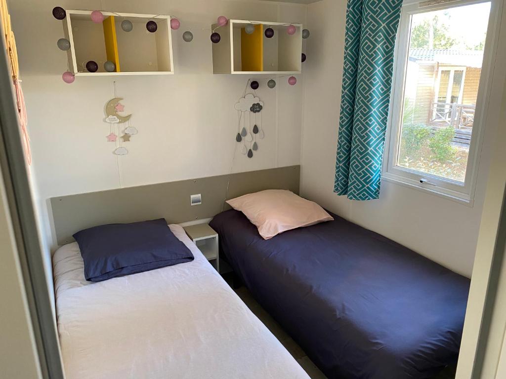deux lits dans une petite pièce avec une fenêtre dans l'établissement Mobil-Home Camping Club 5* Montalivet, à Vendays-Montalivet