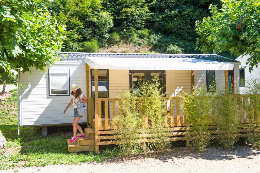 Une femme debout sur la terrasse couverte d'une petite maison dans l'établissement Camping Le château du gibanel, à Saint-Martial-Entraygues