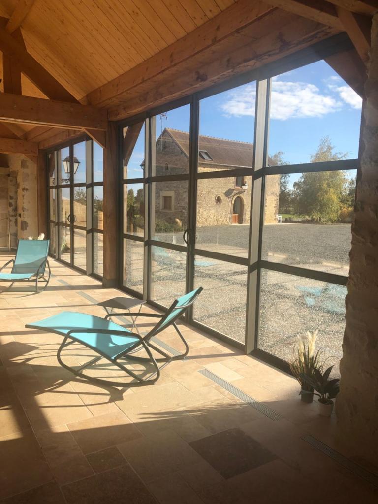 d'une terrasse avec 2 chaises, une table et des fenêtres. dans l'établissement MAISON DE VACANCES AVEC PISCINE INTERIEURE - Le Grand Champagne, à Saint-Victeur