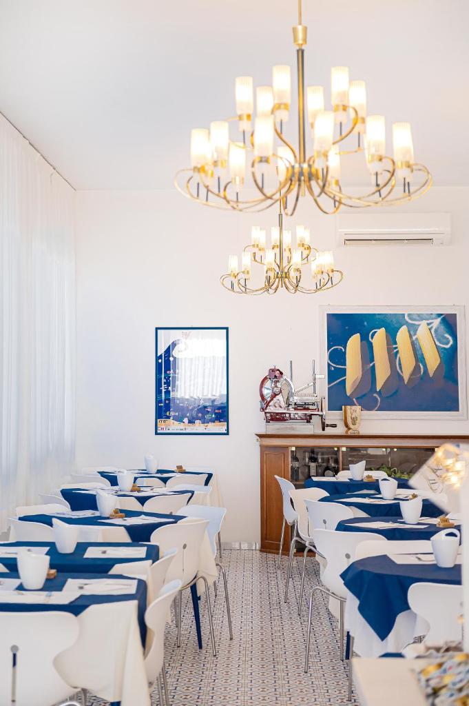 une salle à manger avec des tables blanches et un lustre dans l'établissement Hotel City, à Milano Marittima