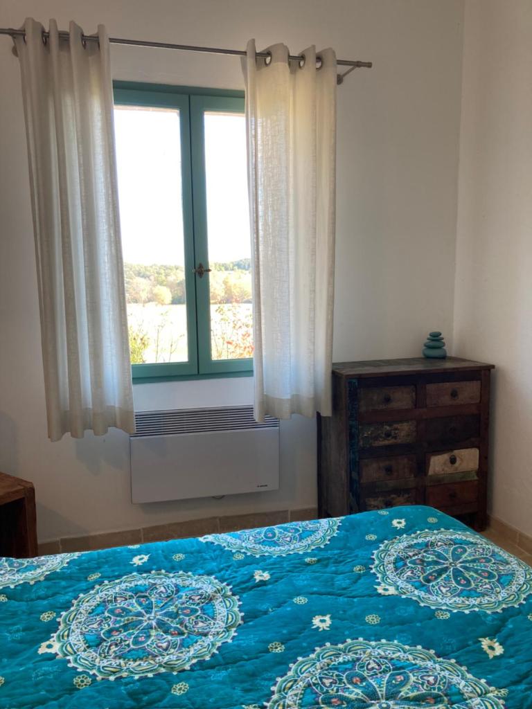 une chambre avec un lit avec une couette bleue et une fenêtre dans l'établissement Le Gîte d'Olves, à Ampus