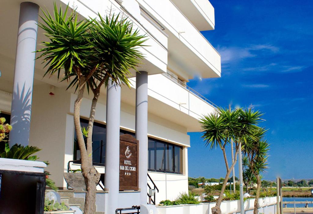 un bâtiment avec des palmiers devant dans l'établissement Hotel Baia del Cigno, à Torre San Giovanni
