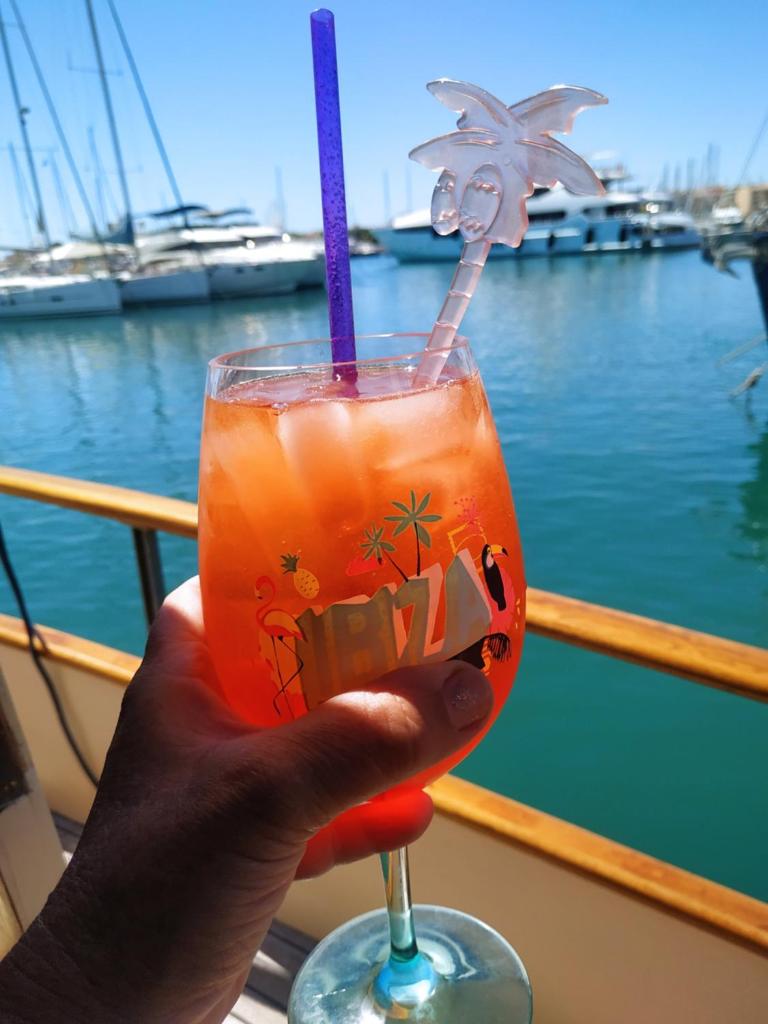 une main tenant une boisson avec une paille violette dans l'établissement Ferretti 36 ' Bateau à Quai Vieux-Port Cannes Festival La Croisette, à Cannes
