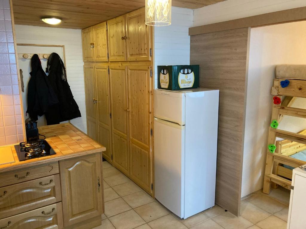 La cuisine est équipée d'un réfrigérateur blanc et de placards en bois. dans l'établissement Appartement 2 pièces pieds des pistes terrasse face à la montagne, à Bernex