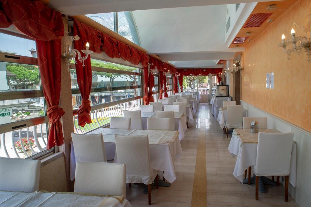 un restaurant avec des tables blanches, des chaises blanches et des fenêtres dans l'établissement Hotel Margherita, à Lido di Jesolo