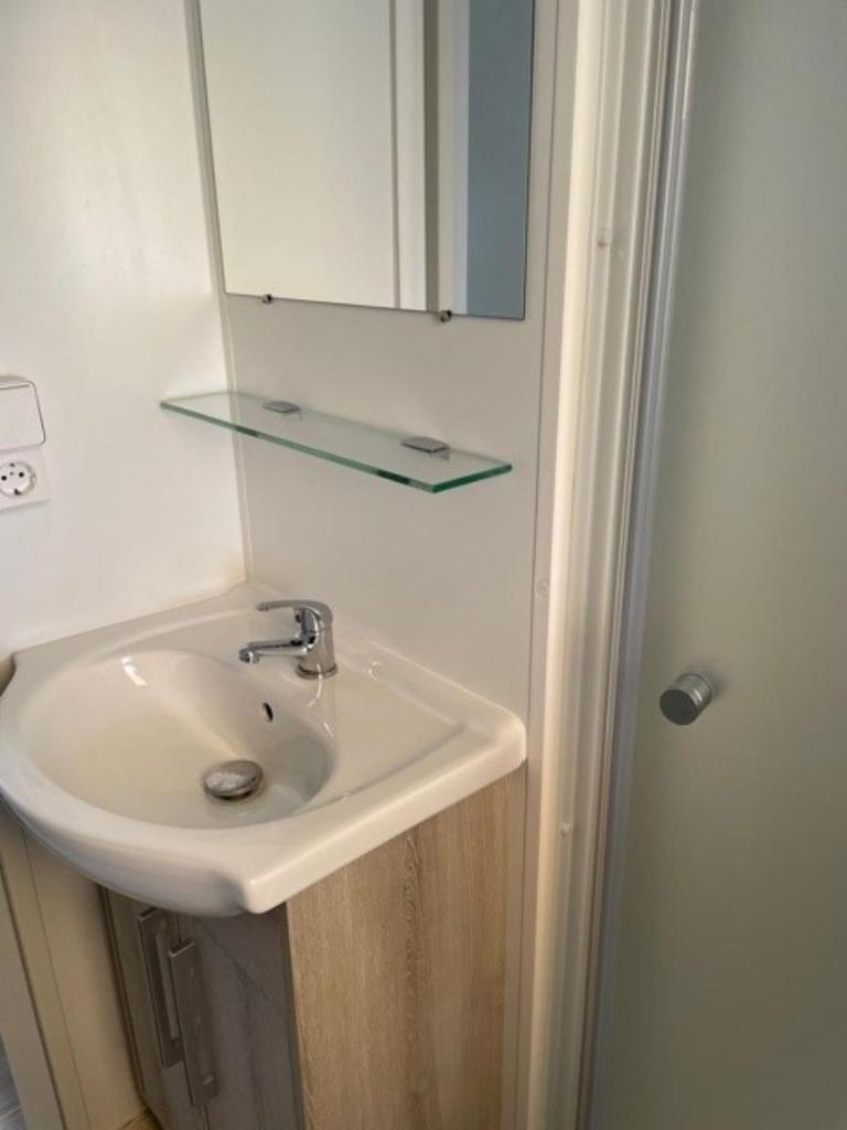 La salle de bains est pourvue d'un lavabo avec miroir et d'une étagère en verre. dans l'établissement Mobil Home, à Fréjus