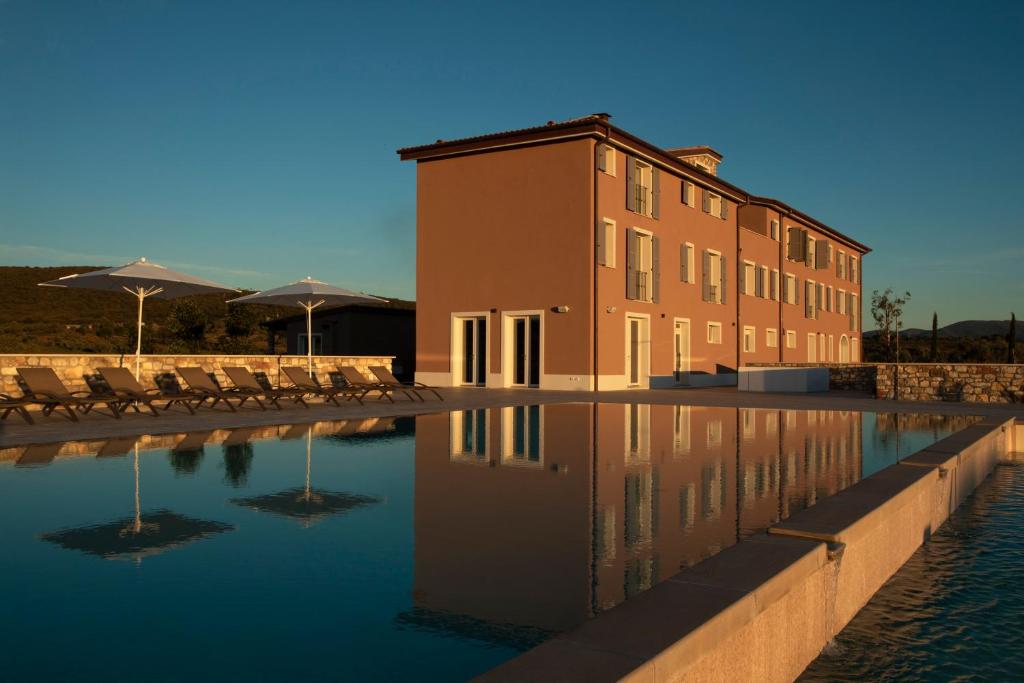 un bâtiment à côté d'un bassin d'eau avec des chaises et des parasols dans l'établissement Riva Toscana Golf Resort & SPA, à Follonica