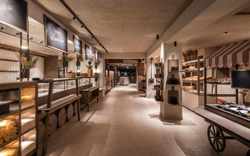 un couloir de magasins avec une boulangerie dotée de comptoirs et de tables dans l'établissement Falkensteiner Family Resort Lido Superior, à Chienes