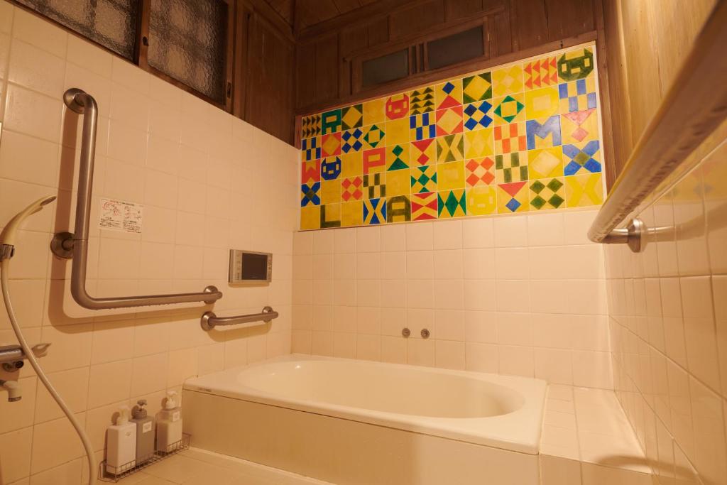 La salle de bains est pourvue d'une baignoire et d'un mur en carrelage coloré. dans l'établissement Ryokan Plum, à Odawara