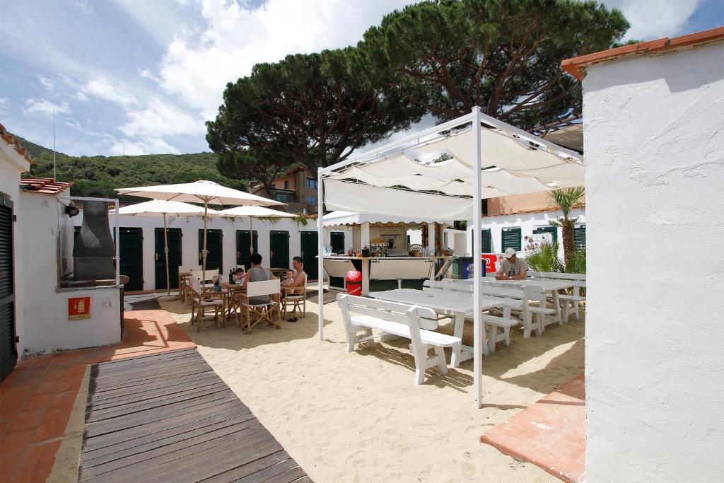 un patio avec des tables et des parasols blancs sur la plage dans l'établissement Hotel Valle Verde, à Procchio