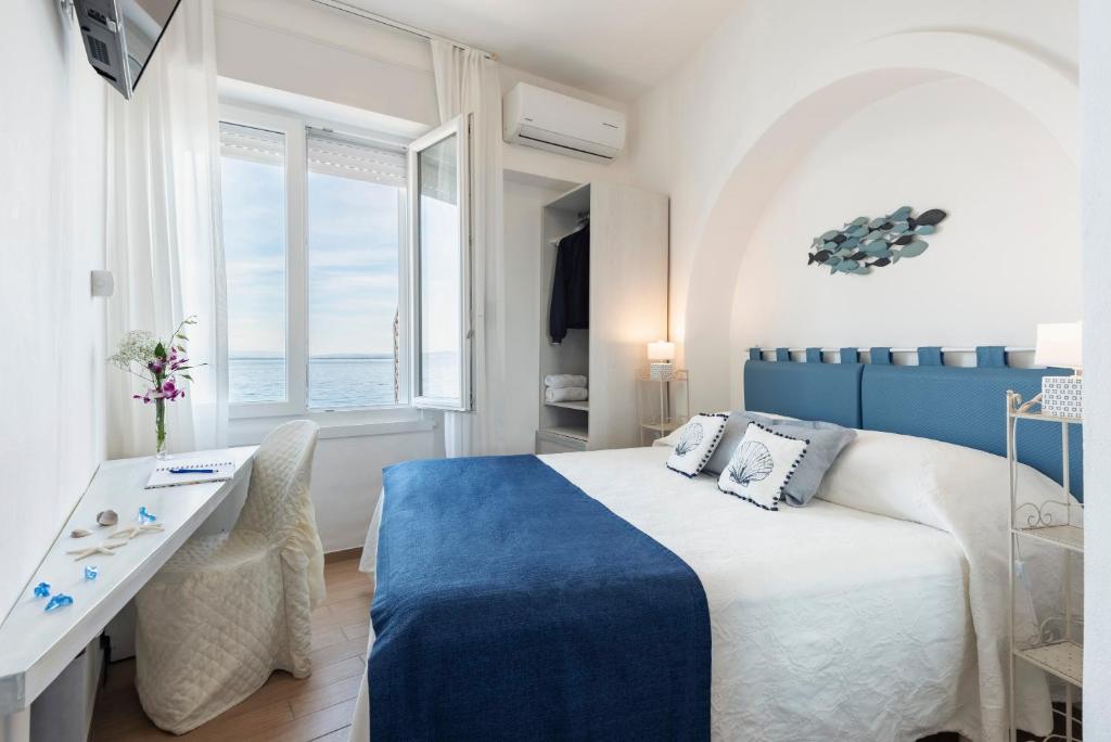 une chambre blanche et bleue avec un lit et un bureau dans l'établissement Hotel La Caletta, à Porto Santo Stefano