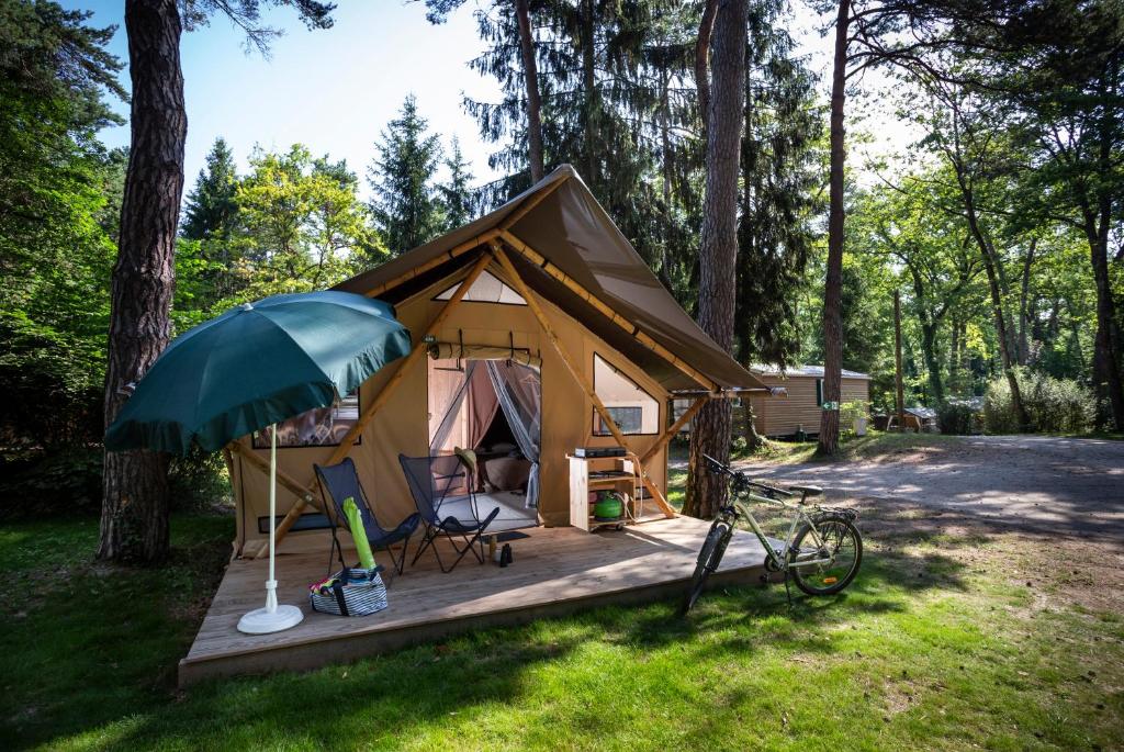 une tente avec un parasol, des chaises et un vélo dans l'établissement Huttopia Lac de Serre-Ponçon, à Le Lautaret