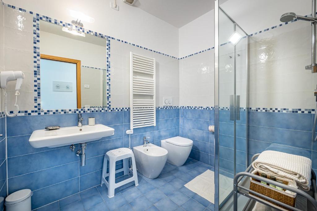 La salle de bains est pourvue de carrelage bleu, d'un lavabo et de toilettes. dans l'établissement Mareblù - Tuscany Green Aparthotel, à Principina a Mare