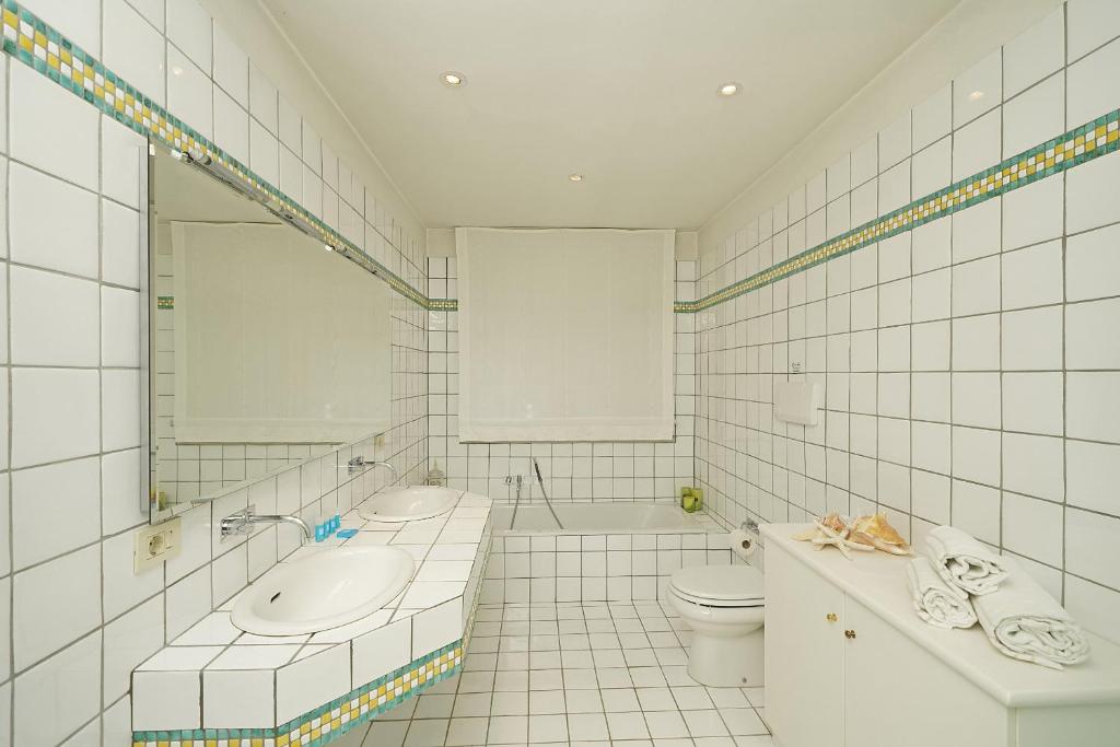 La salle de bains est pourvue de carrelage blanc, d'un lavabo et de toilettes. dans l'établissement Villa Madeleine, à Padenghe sul Garda
