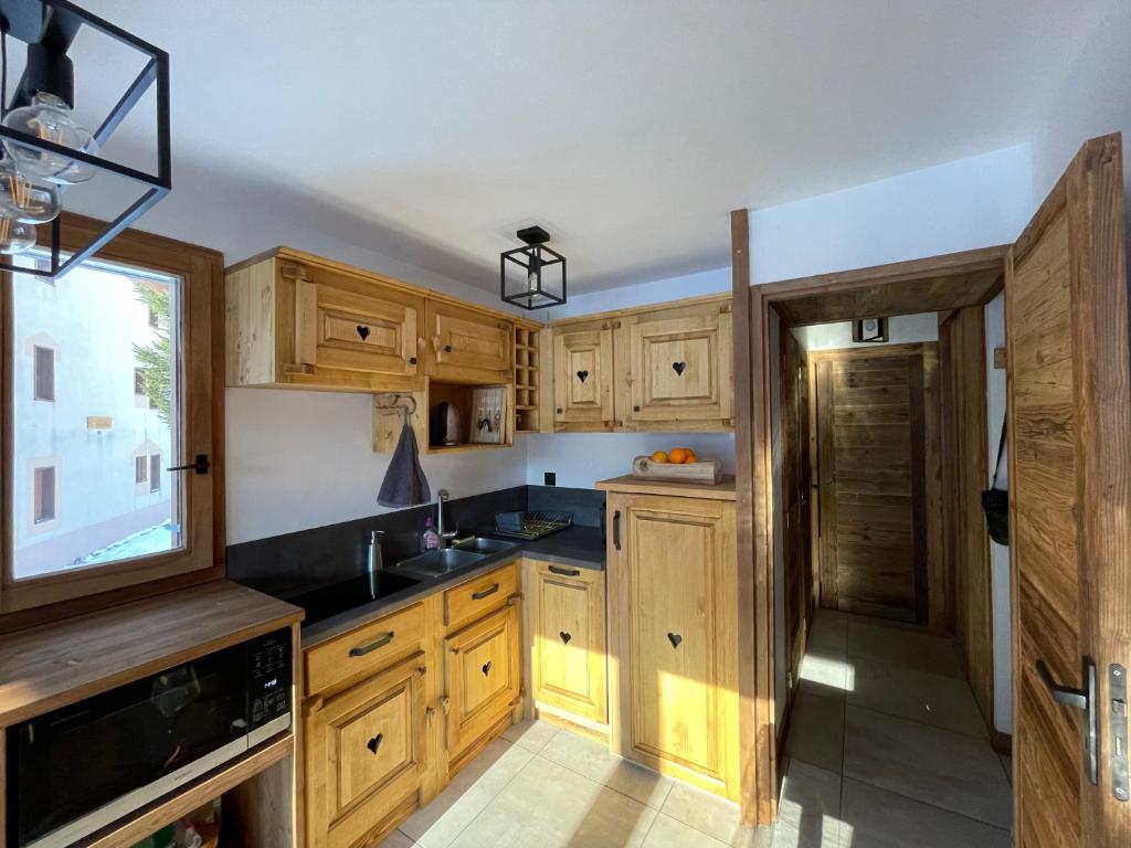une cuisine avec des armoires en bois, un évier et une fenêtre dans l'établissement Le Bouquetin 73 Appartement cosy type chalet avec piscine au pied des pistes et superbe vue panoramique, à Pralognan-la-Vanoise