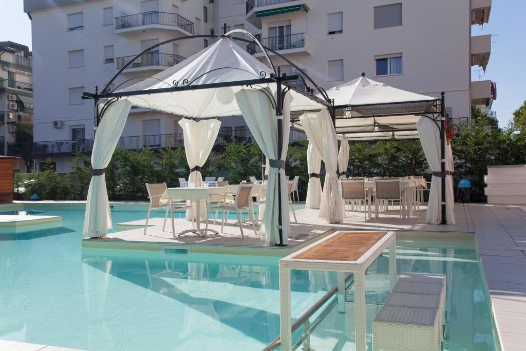 une piscine avec des tables et des parasols à côté d'un bâtiment dans l'établissement Ute Hotel, à Lido di Jesolo