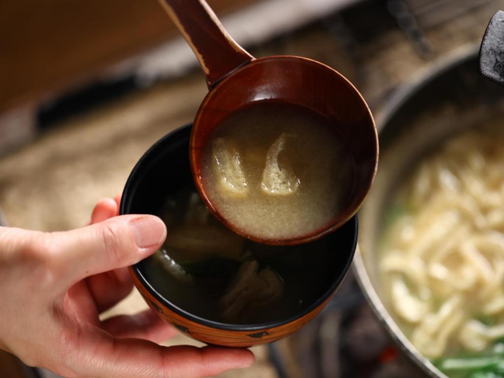 une personne tenant une cuillère en bois à côté d'un bol de soupe dans l'établissement Hotel Yamabuki, à Komagane 37 autres photos