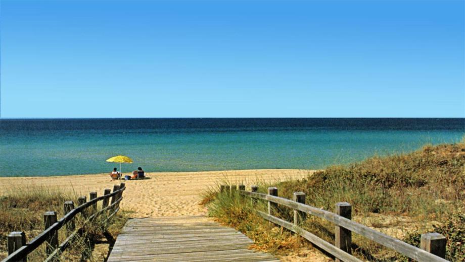 une passerelle en bois menant à une plage avec 2 personnes assises sous un parasol dans l'établissement Albergo 2 Mari, à Leuca