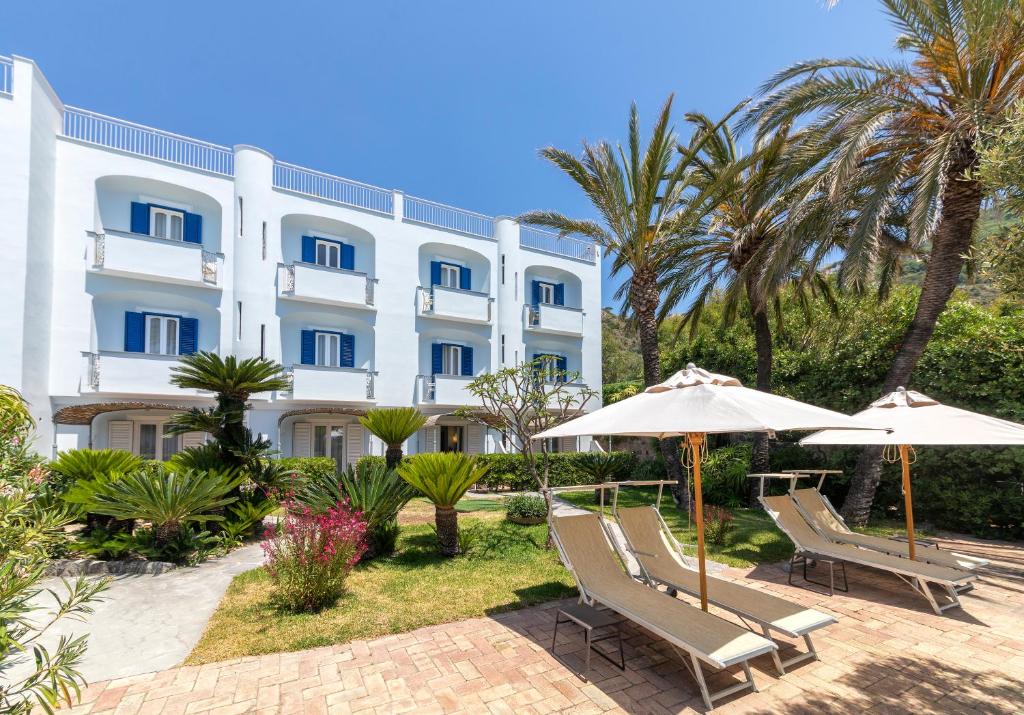 un hôtel avec deux chaises, un parasol et des palmiers dans l'établissement Hotel Parco Smeraldo Terme, à Ischia