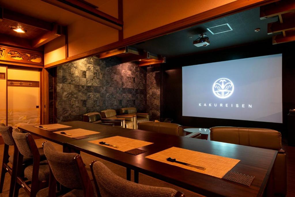une salle de conférence avec un écran de projection, des tables et des chaises dans l'établissement Kakureisen, à Saga