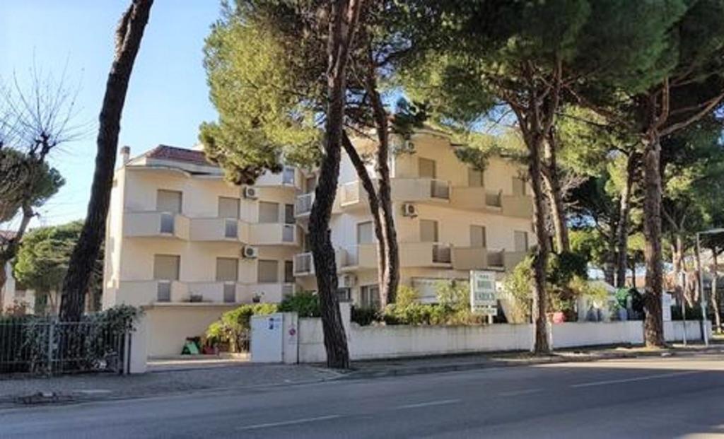 un grand bâtiment avec des arbres en face d'une rue dans l'établissement Hotel Enrica, à Cervia
