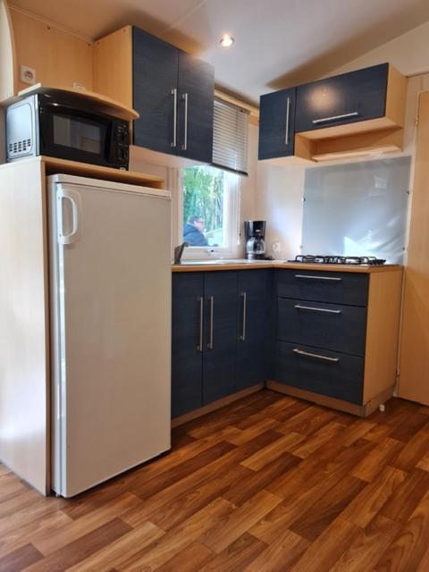 La cuisine est équipée de placards bleus et d'un réfrigérateur blanc. dans l'établissement MOBIL HOME familiale EN ALSACE11 KM DES GRANDS PARCS, à Boofzheim
