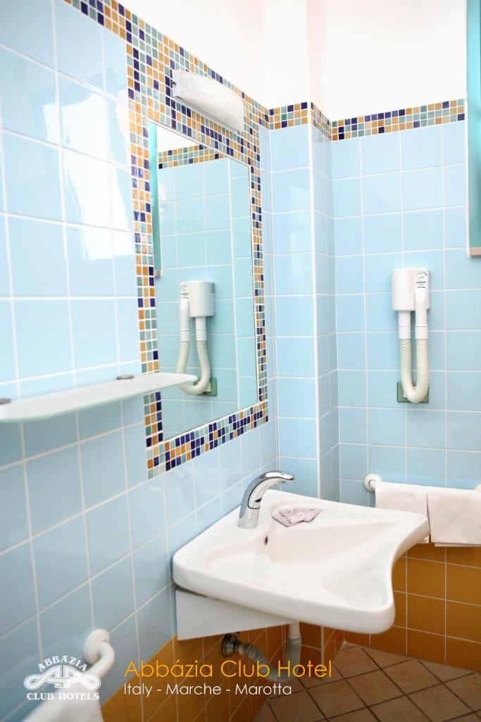 La salle de bains est pourvue de carrelage bleu, d'un lavabo et d'un miroir. dans l'établissement Abbazia Club Hotel Marotta, à Marotta