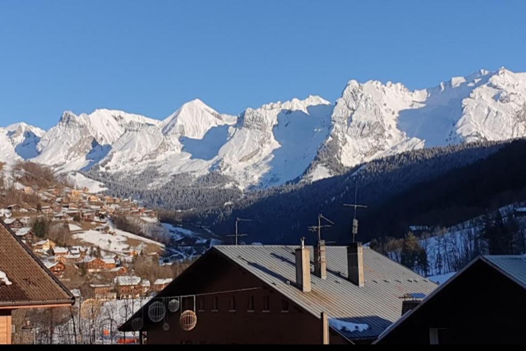 une église avec des montagnes enneigées en arrière-plan dans l'établissement Studio with balcony in the center of the village, au Grand-Bornand