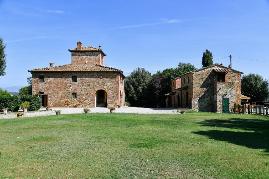 un ancien bâtiment en pierre avec une pelouse devant lui dans l'établissement Casale le Rondini by VacaVilla, à Lucignano