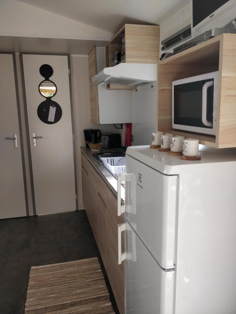 La cuisine est équipée d'un réfrigérateur blanc et d'un four micro-ondes. dans l'établissement Mobile-Home 6 personnes Cap Ferret, à Claouey